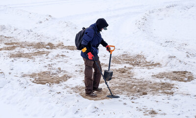 Treasure hunter is looking for treasures on the winter snow with a metal detector.