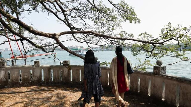 Tourists Indian Mother and daughter walking along the sea shore in Fort Kochi beach on summer vacation Kerala India 4K slow motion video footage. outing  in coastal region walkway.