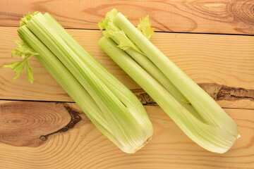 Two light green natural, juicy stalks of celery on a wooden table, close-up, top view.