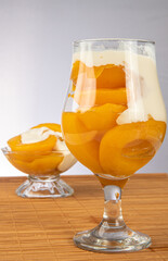 Peaches in syrup placed in two bowls covered with sour cream on wooden mat, gray gradient background, selective focus.