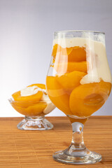 Peaches in syrup placed in two bowls covered with sour cream on wooden mat, gray gradient background, selective focus.