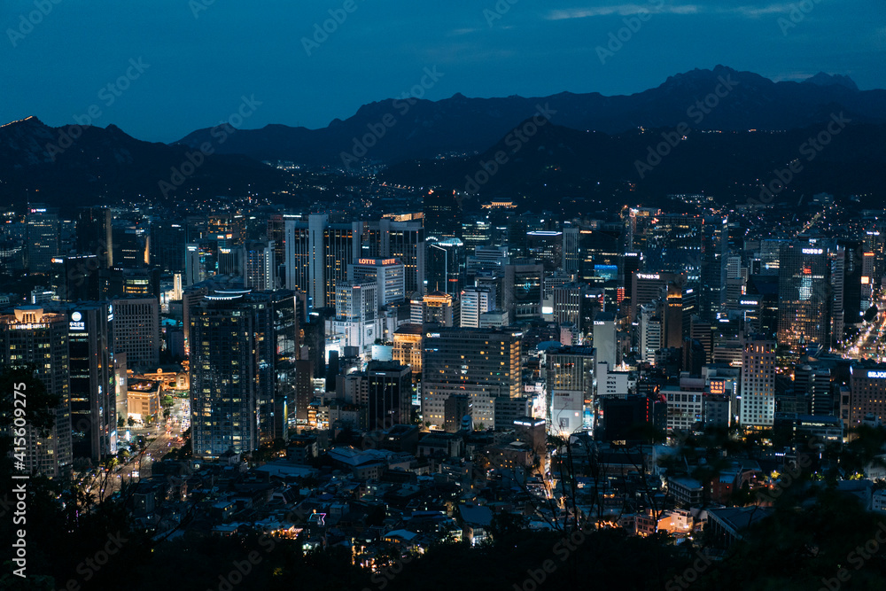 Wall mural Cityscape of Seoul, South Korea lit up at dusk, with Mountains behind.