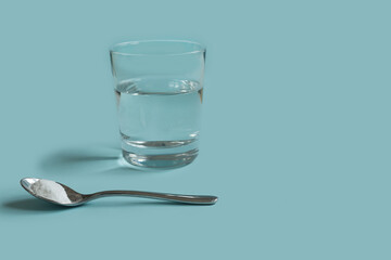 collagen soluble powder in spoon  and water glass on a light blue background