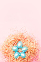 Happy easter background, colored pearl blue eggs in hay nest over bright pink color