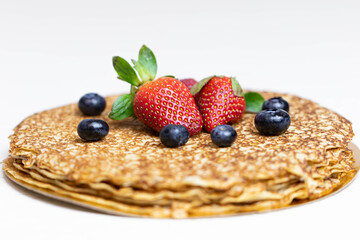 Ripe juicy strawberries and blueberries lie on a delicious pancake. Russian cuisine national dish bliny with fresh berries.