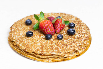 Ripe juicy strawberries and blueberries lie on a delicious pancake. Russian cuisine national dish bliny with fresh berries.