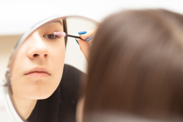 Young woman applies makeup looking in the mirror, combs her eyelashes with a brush