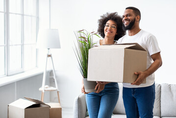 Black Couple Holding Packed Boxes Moving New House Standing Indoors