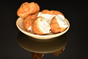 Tasty chouquettes with cream on a saucer, on a black background.