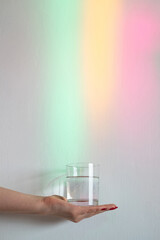Clear water. Reflection rainbow light. Healthy life. Organic natural. Female hand holding glass clean beverage isolated on blur neon light glowing rays background.