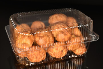 Several delicious chouquettes in a plastic box on a black background.