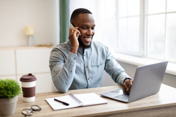 Obraz premium African Businessman Talking On Phone Sitting At Laptop In Office