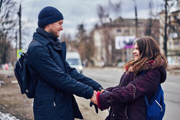 Young lovers in warm clothes hold each other's hands on a city street.
