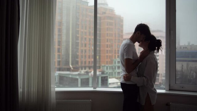 Enamored man and woman of Caucasian ethnicity at the window, kiss. Concept of love.