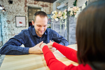 The guy holds the girl's hands and looks at them in a cafe.