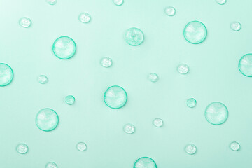 Liquid gel cosmetic on blue. Texture of drops gel on mint background. Pattern of transparent drops gel for face cleansing. Moisturizing cosmetic beauty product for skincare. Serum for skin care
