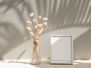 Blank mockup picture frame and dried flower in glass vase on beige table and background