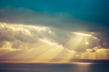 Fototapeta na wymiar A dramatic sunset through the clouds over the ocean with rays of light piercing the clouds.
