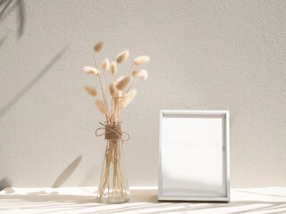 Blank mockup picture frame and dried flower in glass vase on beige table and background