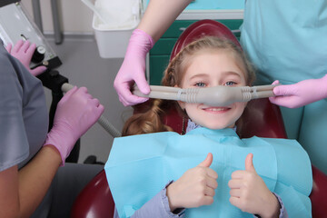 A little girl is comfortable to treat her teeth under superficial sedation. The girl smiles and...