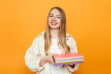 Happy caucasian female student holds a lot of books isolated over orange studio background. Education concept. College student girl smiling at camera