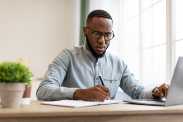 Black Businessman Taking Notes Sitting Working At Workplace In Office
