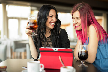 two pretty women looking tablet in bar while drinking coke and coffee