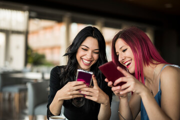 Two women looking smartphones in bar and sharing photos 