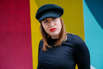 Portrait of a Caucasian woman with beret, smiling, with an angry expression. A colorful wall of the street in the background. Party, positivity and self-improvement concept.