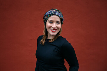 Portrait of a Caucasian woman with headscarf, smiling . A red wall of the street in the background. Art and women concept. Copyspace