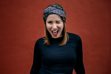 Portrait of a Caucasian woman with headscarf, smiling and winking . A red wall of the street in the background. Art and women concept. Copyspace