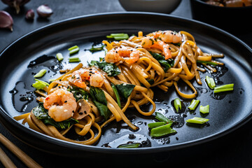 Asian food - noodles with prawns in soy sauce with spinach on black table