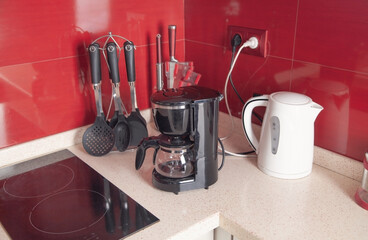 Set of cookware, white kettle and black coffee maker machine in kitchen.