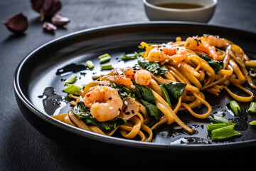 Asian food - noodles with prawns in soy sauce with spinach on black table