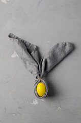 Creative Easter bunny - yellow egg in a gray napkin on a concrete background, vertical background, flat layout