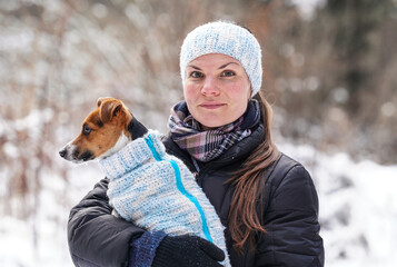 Young woman in winter jacket holding her Jack Russell terrier dog wearing warm winter clothing on...