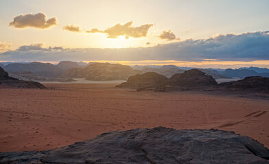 Wadi Rum desert in Jordan, rocky mountains with flat sand field around, afternoon sunset clouds background
