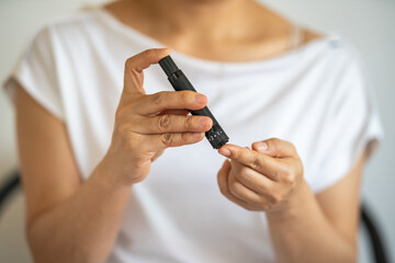 Fototapeta premium Close up of woman hands using lancet on finger to check blood sugar level by Glucose meter. Use as Medicine, diabetes, glycemia, health care and people concept.