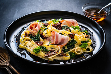 Tagliatelle with bacon, sun-dried tomatoes and spinach in alfredo sauce on black wooden table 
