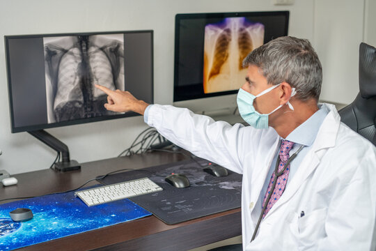 Confident male doctor wearing mask and looking to computer screen x-ray image in pandemic time