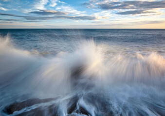 A closeup shot of a wavy sea against the rocks under a sunset sky