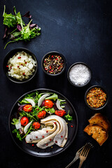 Marinated herrings with roast cherry tomatoes and fresh vegetable leaves on black table
