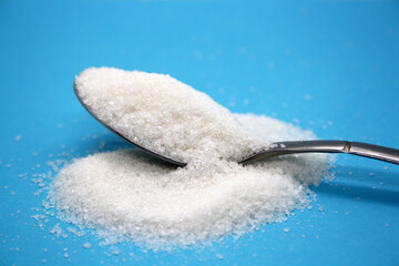 Sugar poured into a spoon on a blue background.