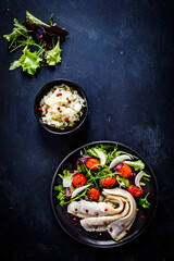 Marinated herrings with roast cherry tomatoes and fresh vegetable leaves on black table
