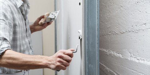 closeup hands man drywall worker or plasterer putting stucco on plasterboard wall using a trowel and a spatula, fill the screw holes