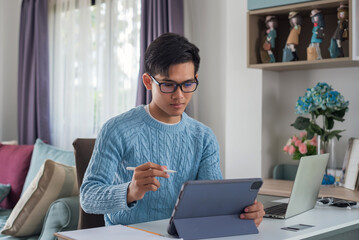 Young Asian man sitting at home working on a tablet