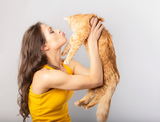 Happy young woman kissin and holding on the hands her red maine coon kitten and kissing. Closeup portrait