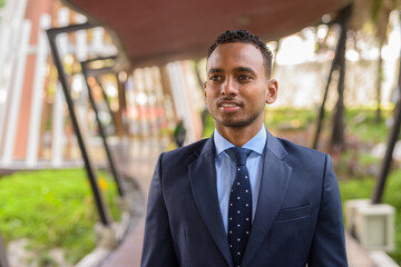 African businessman wearing suit and smiling outdoors while thinking and looking away