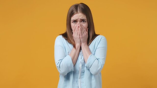 Shocked worried scared blonde young woman 20s years old in casual blue shirt posing isolated on yellow background studio. People sincere emotions lifestyle concept. Covering face with hands hiding