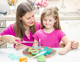 Cute little girl blowing out candles with mom on birthday cake muffin at home